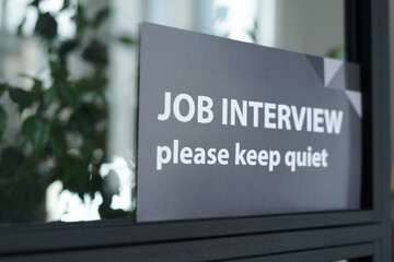Close-up of black sign warning about job interview in behind glass door in modern office