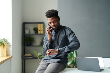African American businessman having a conversation on mobile phone while checking time on his watch, he waiting for meeting with colleague