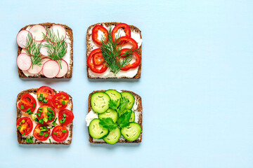 Variety of sandwiches for breakfast - slice of whole grain dark bread, pepper, cream cheese, cucumbers, radishes, cherry tomatoes, garnished with dill, green onions on blue table Top view Flat lay - 569797435