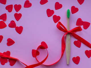 Flat lay with a lot of tiny heart-shaped papers, toothbrush and space for text. Red heart paper background with toothbrush tied with a red bow. Valentines day dentist concept. February 14th.