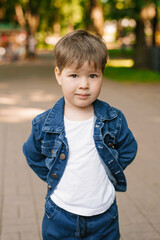 Portrait of a cute three-year-old boy in jeans in summer in the park