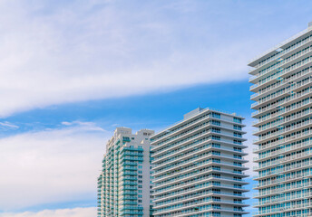 Fototapeta premium Row of modern apartments in Miami, Florida under the giant flat clouds in the sky. Three high-rise apartments with glass balcony railings.
