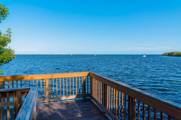 Fototapeta na wymiar View from a corner of a boardwalk near the Dinner Key Marina at Miami, Florida. Wooden path with railings with a view of the blue ocean waters and clear sky background.