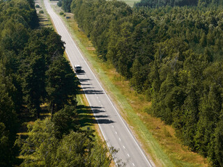 Moving cars on highway between green forests among fields