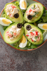 Avocado Filled with Chicken Salad served with boiled eggs and lettuce closeup on the plate on the table. Vertical top view from above