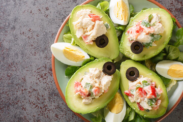 Chilean appetizer of ripe avocados stuffed with chicken salad on a bed of leafy greens close-up on a plate on the table. Horizontal top view from above