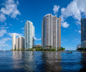 Fototapeta na wymiar Miami, Florida- Coastal modern high-rise buildings against the sky background. There is a reflective water at the front with boat on the right near the buildings.