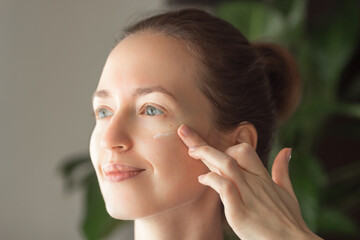 Portrait of beautiful young woman smiling and applying moisturizing face cream or lotion with finger. Skin care concept.