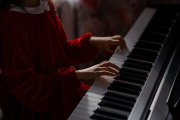 Fototapeta na wymiar A little girl in a red velvet dress plays the electronic piano