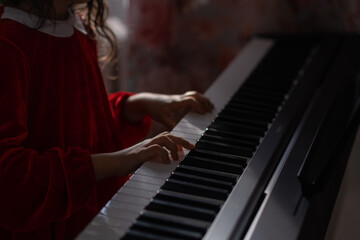 Fototapeta na wymiar A little girl in a red velvet dress plays the electronic piano