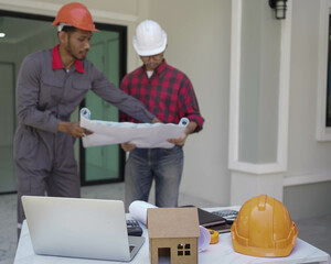 Smiling young architect or engineering builder in hard hat with tablet over group of builders at...