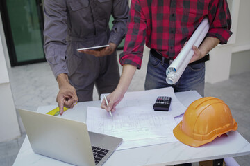 Smiling young architect or engineering builder in hard hat with tablet over group of builders at...
