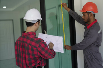 Smiling young architect or engineering builder in hard hat with tablet over group of builders at...