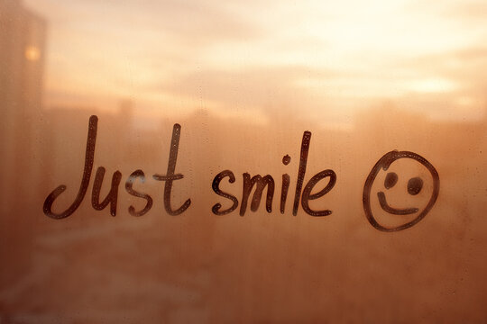 lettering text Just smile and happy smile painted on window flooded with raindrops on orange glass background in city