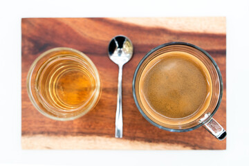 Crema of black coffee in a clear glass on a wooden tray, with a clear tea glass next to it selective focus, soft focus.           