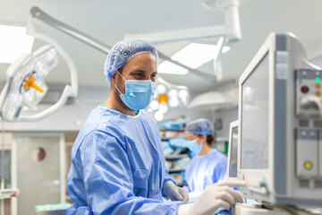 Anesthetist Working In Operating Theatre Wearing Protecive Gear checking monitors while sedating...