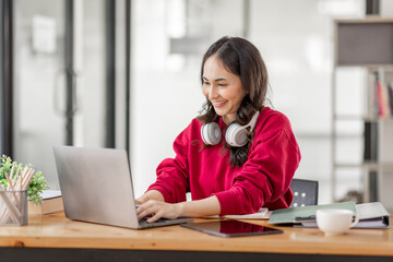 Portrait of Young asian woman wearing headphones using laptop in cafe, writing notes, learning language, watching online business or education concept