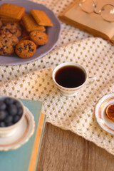 Plate of cookies, cup of tea, fresh blueberries, dry oranges, stack of books, reading glasses and tablet on the table. Hygge at home. Selective focus.