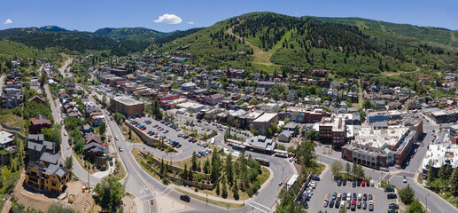Scenic residential community in the mountains of Park City Utah on a sunny day. Aerial view of houses, buildings, roads, and cars against trees and green field with blue sky.