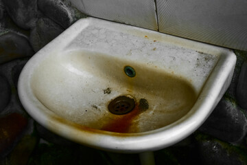 close up view of the dirty stain inside of the toilet sink in the house. Yellow limescale stain. garbage from one white old ceramic washstand sink in brown dirt.