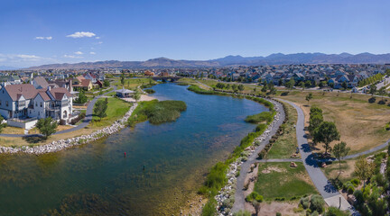 Fototapeta na wymiar Panorama aerial view of Daybreak community in Utah with lake in the middle with pathways on the side. There are houses surrounding the lake with grassy shore and pathways on the side.