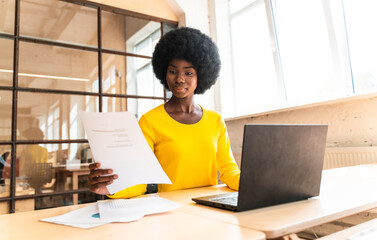 beautiful woman with curly afro haircut and yellow top working in the office