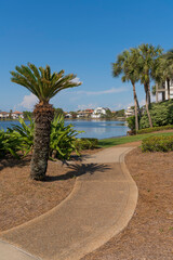 Curved concrete pathway with plants and views of Four Prong Lake and houses at Destin, Florida. Pathway near the residential area surrounding the lake in a vertical shot view.
