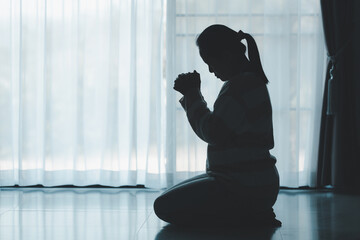 silhouette of woman kneeling and praying in modern church at sunset time. Female catholic prayer...
