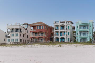 Beach houses with roof decks and balconies with views of white sand shore in Destin, Florida. There are white sand at the front near the dunes with grasses and footbridge above.