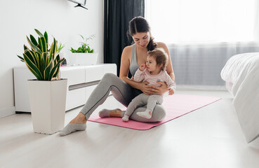 Young sporty mother and baby girl working out, exercising together at home, parent and child...