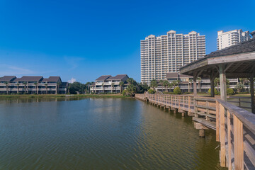 Fototapeta na wymiar Residential area with waterfront views and boardwalk in Destin, Florida. There is a boardwalk with gazebo on the right over the water against the modern apartments and blue sky at the background.
