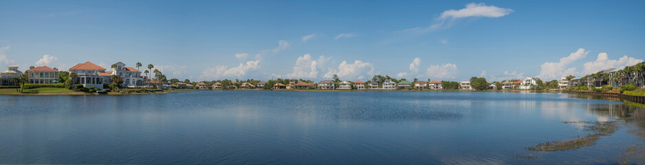 Fototapeta na wymiar Four Prong Lake waterfront at Destin, Florida panorama. Large residential family houses with lake waterfront against the blue sky with puffy clouds.