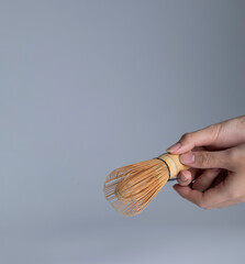 Hand holding matcha whisk on white background.
