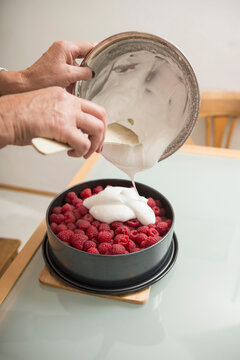 Senior woman pouring meringue on cake base and berries in springform pan, Munich, Bavaria, Germany