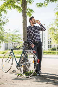 Young man leaning against a tree and drinking coffee, Munich, Bavaria, Germany