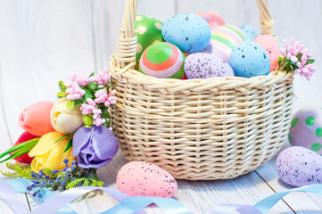 basket with painted Easter eggs and spring flowers on a light wooden background, Easter card. High quality photo