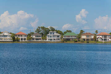Fototapeta na wymiar Facade of single-family homes with views of Four Prong Lake waterfront in Destin, Florida. Row of houses with balconies and fences against the giant pastel clouds in the sky background.
