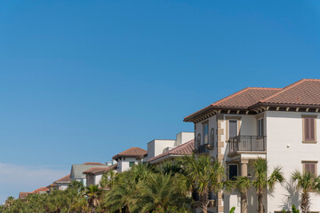 Row of houses with clay tile roofs and palm trees at the front in Destin, Florida. Trees along with the houses against the blue sky background.