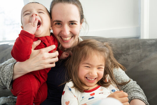 Smiling Mother Holds Her Laughing Son and Daughter at Home