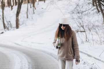 Fototapeta na wymiar Smiling woman with dark hair in winter clothes with paper cup of coffee in hands