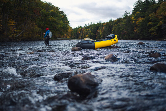A fly-fisherman casting behind a packraft on a river in fall