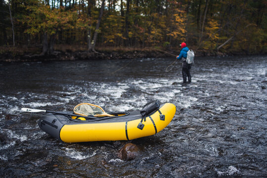 A fly-fisherman casting behind a packraft on a river in fall