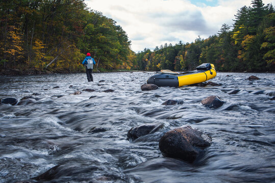 A fly-fisherman casting behind a packraft on a river in fall
