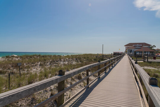 Wooden walkway and beach houses against blue sky in Destin Florida. Relaxing coastal scenery with ocean, blue sky, and waterfront residences on a sunny day.