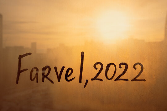 lettering Farvel in Danish is bye in english and numbers 2022 paint with finger of water on splashed by rain foggy glass on sunset window