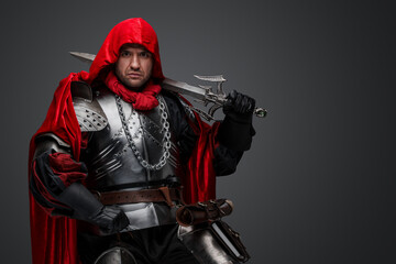 Shot of dark knight dressed in steel armor and red robe against gray background.