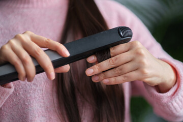 Woman straight hair using hair straightener. Hair ironing and hairstyle concept