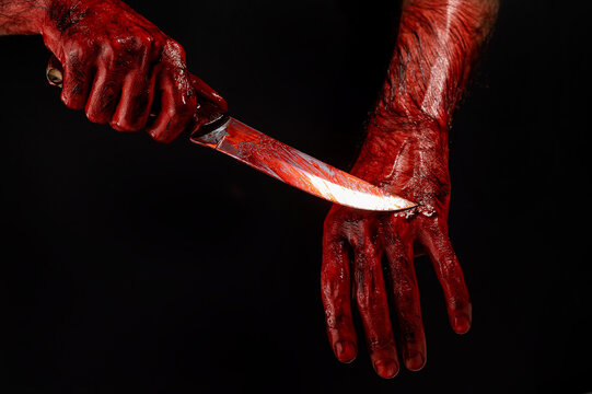 A man wipes a bloody knife with his hand on a black background. 