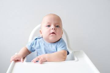 bald smiling baby boy 3 months sitting in baby chair on white background