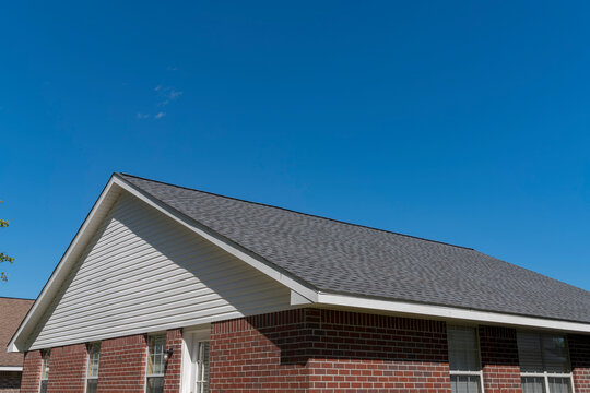 Brick house peak with white wood siding and gray roof against the blue sky in Navarre, Florida. House exterior with wall bricks and white wood house peak.